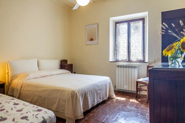Ein Schlafzimmer mit einem Bett, einem Sessel, einem Fenster mit Vorhängen, einer Heizung und einem Wandbild.