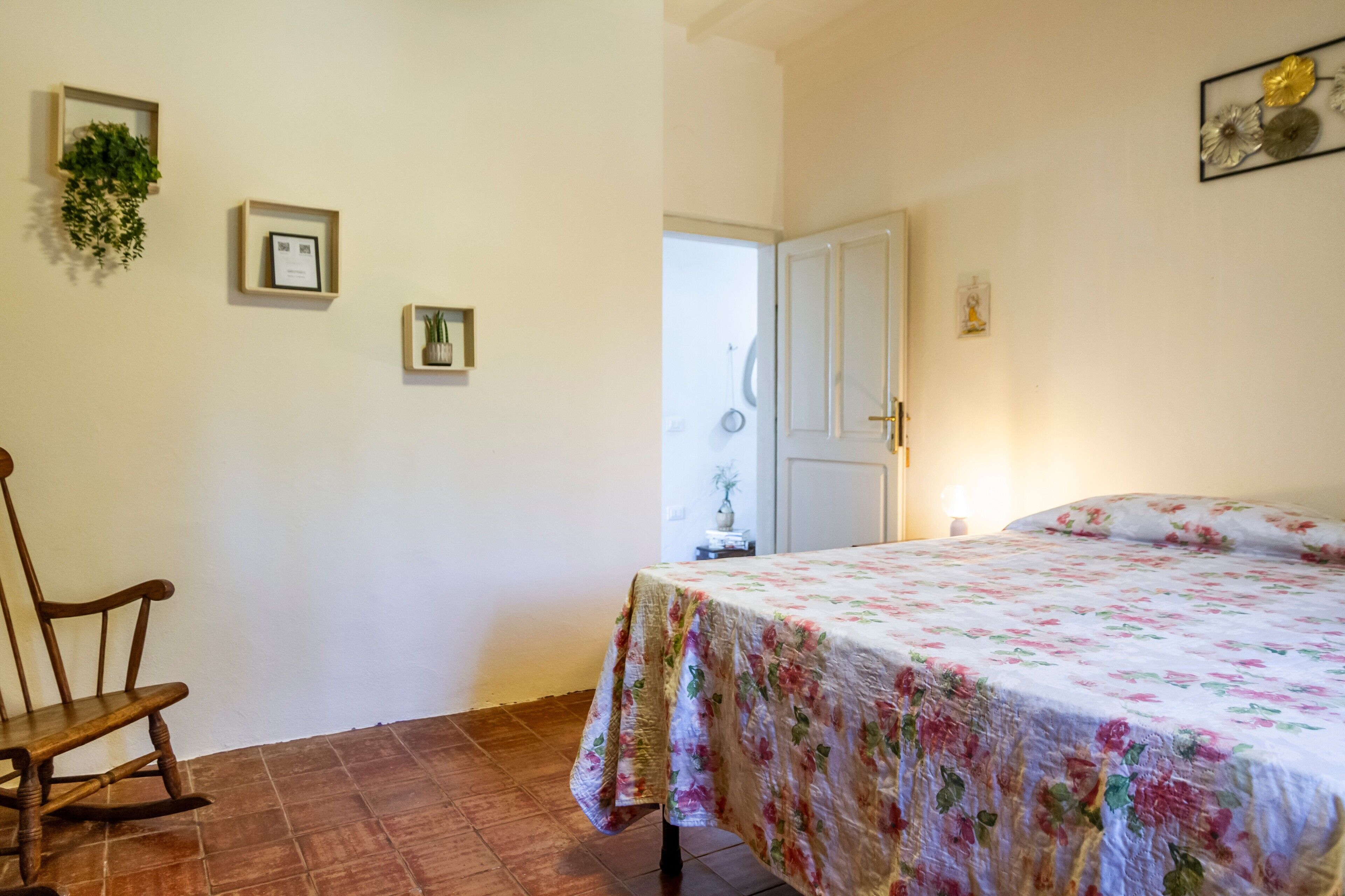 Une chambre à coucher avec un lit, un fauteuil à bascule, une porte et une plante fixée au mur.