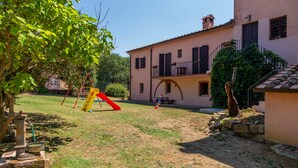 Una casa con balcón, zona de juegos con tobogán y un muro de piedra.