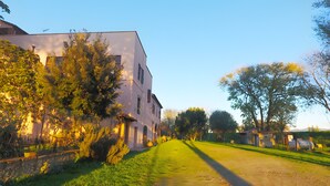 Un edificio con techo inclinado, camino de entrada pavimentado y zona ajardinada con árboles.