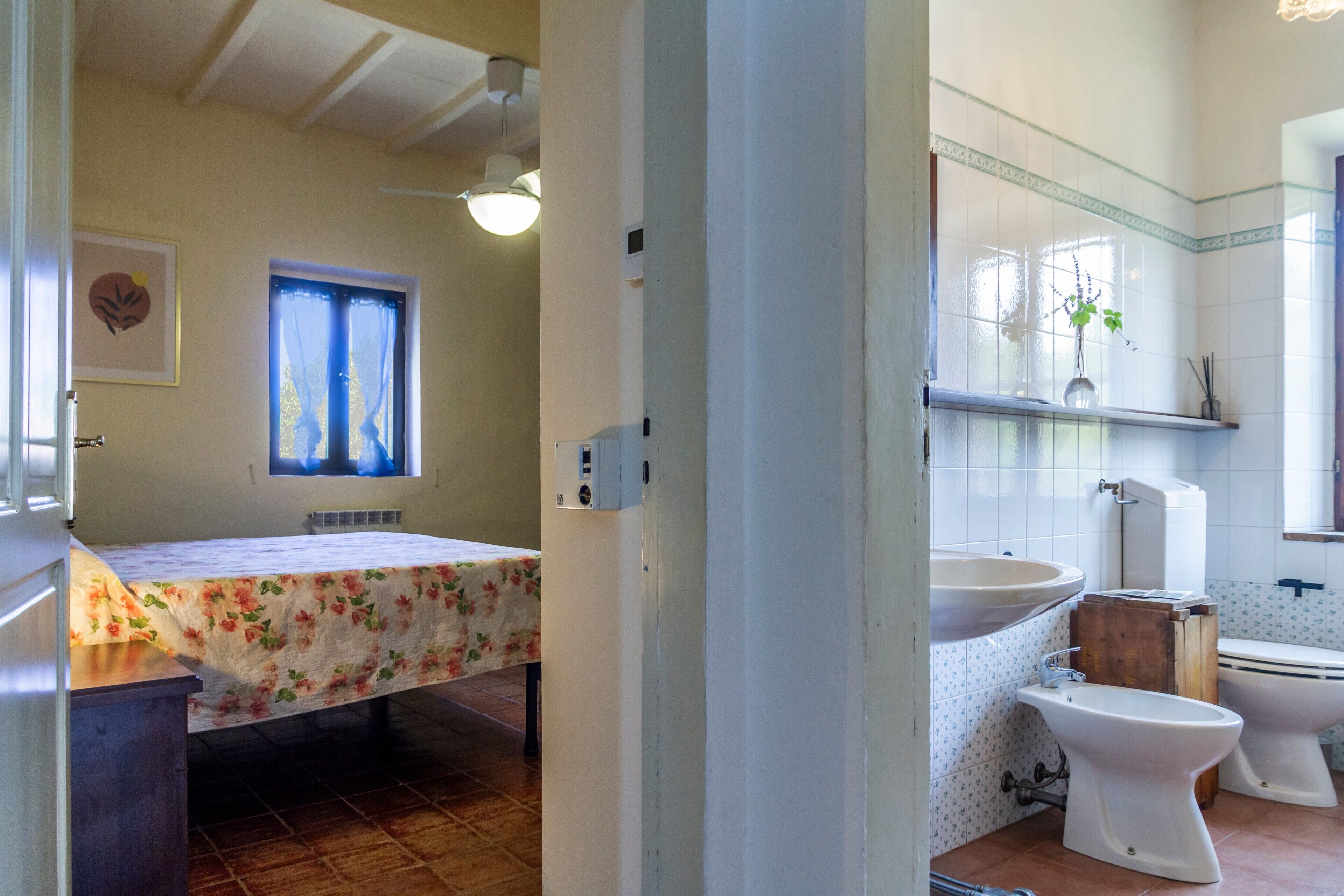 Un baño con cama, lavamanos, dos inodoros y ventana con cortinas.