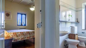 Un baño con cama, lavamanos, dos inodoros y ventana con cortinas.