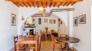 Un comedor con mesas y sillas de madera, una cocina al fondo y un techo rústico.