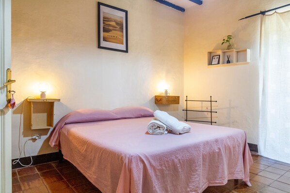 Een slaapkamer met een bed, nachtlampjes, een plank met spullen en een lijst aan de muur.