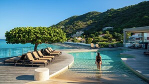 Zona junto a la piscina con sillones de descanso, un árbol y vistas al mar y las colinas.