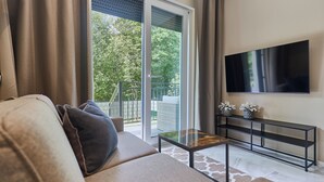 A living room with a sofa, a coffee table, a TV, and a sliding glass door leading to a balcony. - 11 listopada 70 c (Świnoujście)