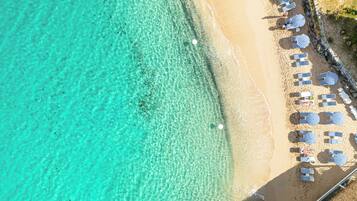 Vista aérea de uma praia com águas turquesas cristalinas, areal dourado e fileiras de guarda-sóis e espreguiçadeiras.