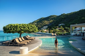A poolside area with lounge chairs, a tree, and a view of the sea and hills. - Garden View Room with Private Beaches, Pool, Gym & Watersports Adventures (Grand-Case)