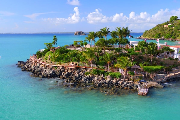 A coastal resort with a wooden walkway, palm trees, and a rocky shoreline.