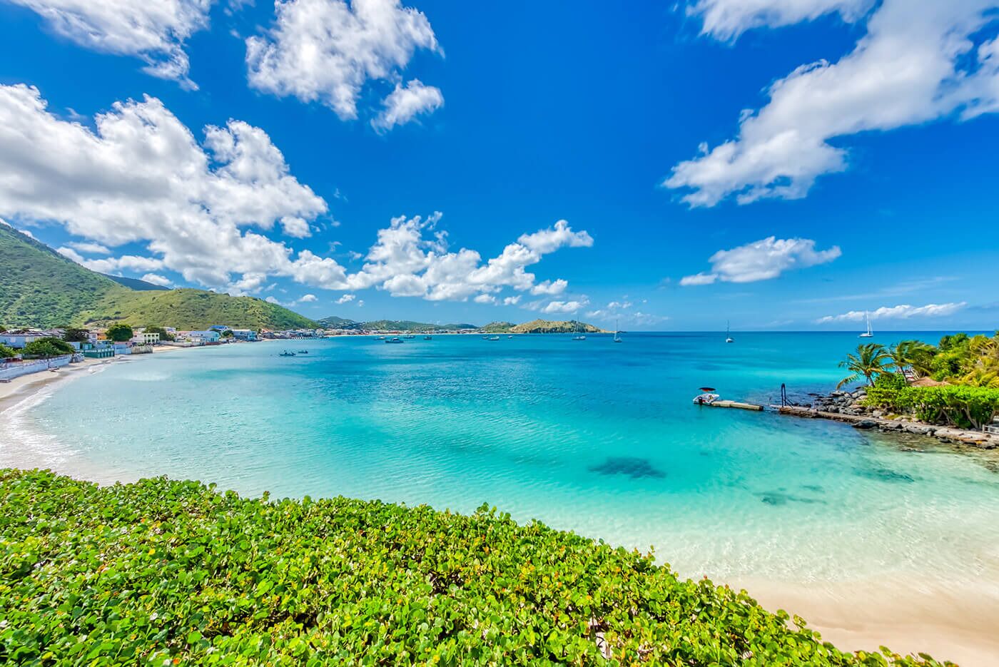 Blick auf die Küste mit klarem türkisblauem Wasser, einem Sandstrand und üppiger Vegetation.