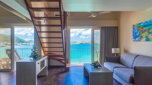A modern living room with a wooden staircase, a sofa, a coffee table, and a view of the sea.