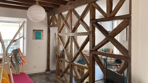 Une pièce avec des poutres apparentes, une lanterne en papier blanche suspendue, un tapis de jeu rose et un téléviseur.