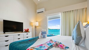 Une chambre d’hôtel comprenant un lit, une télévision, un bureau avec des tiroirs, une lampe et une vue sur l’océan depuis la porte-fenêtre donnant sur le balcon.