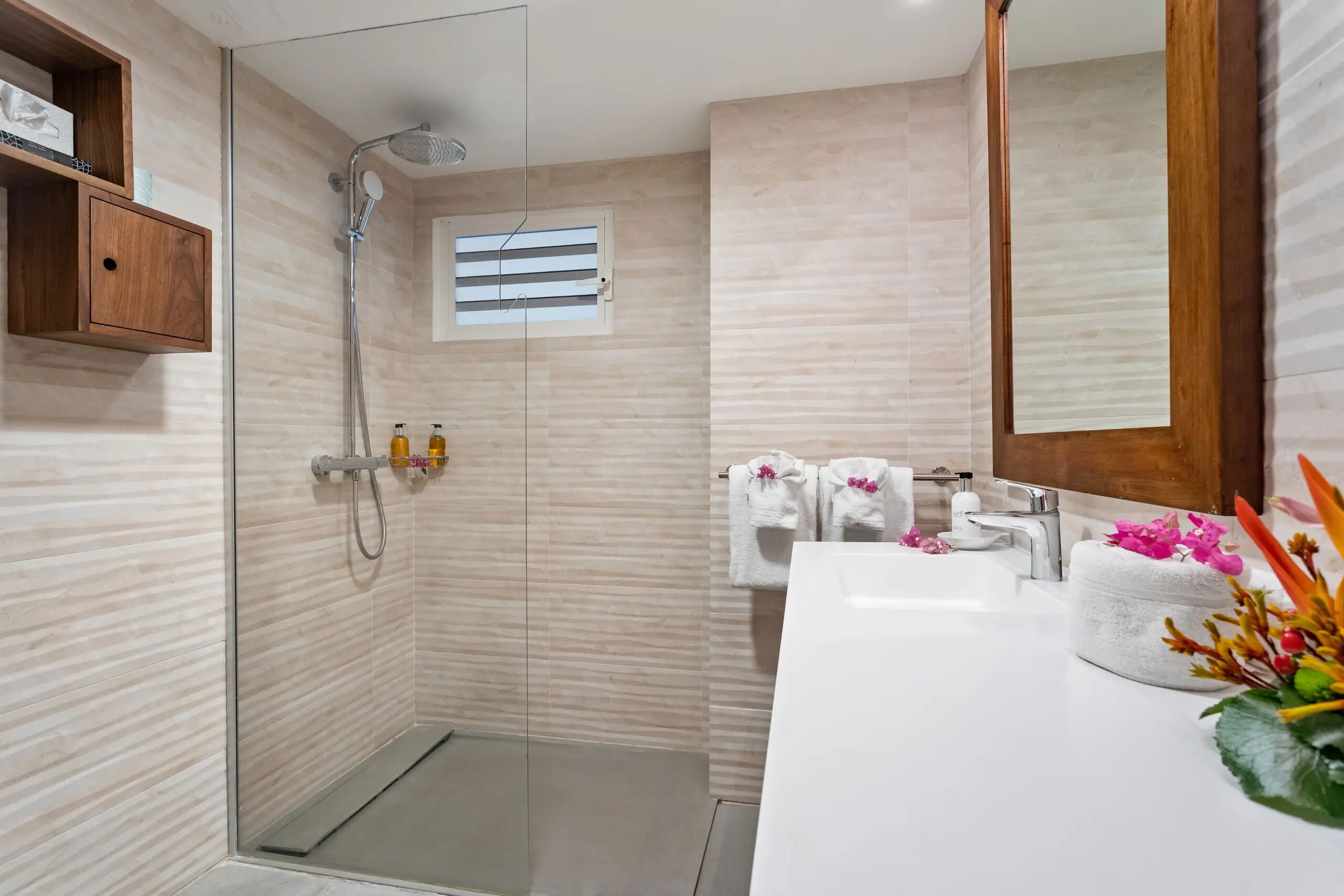 A modern bathroom with a glass-enclosed shower, a white sink, and a wooden shelf.