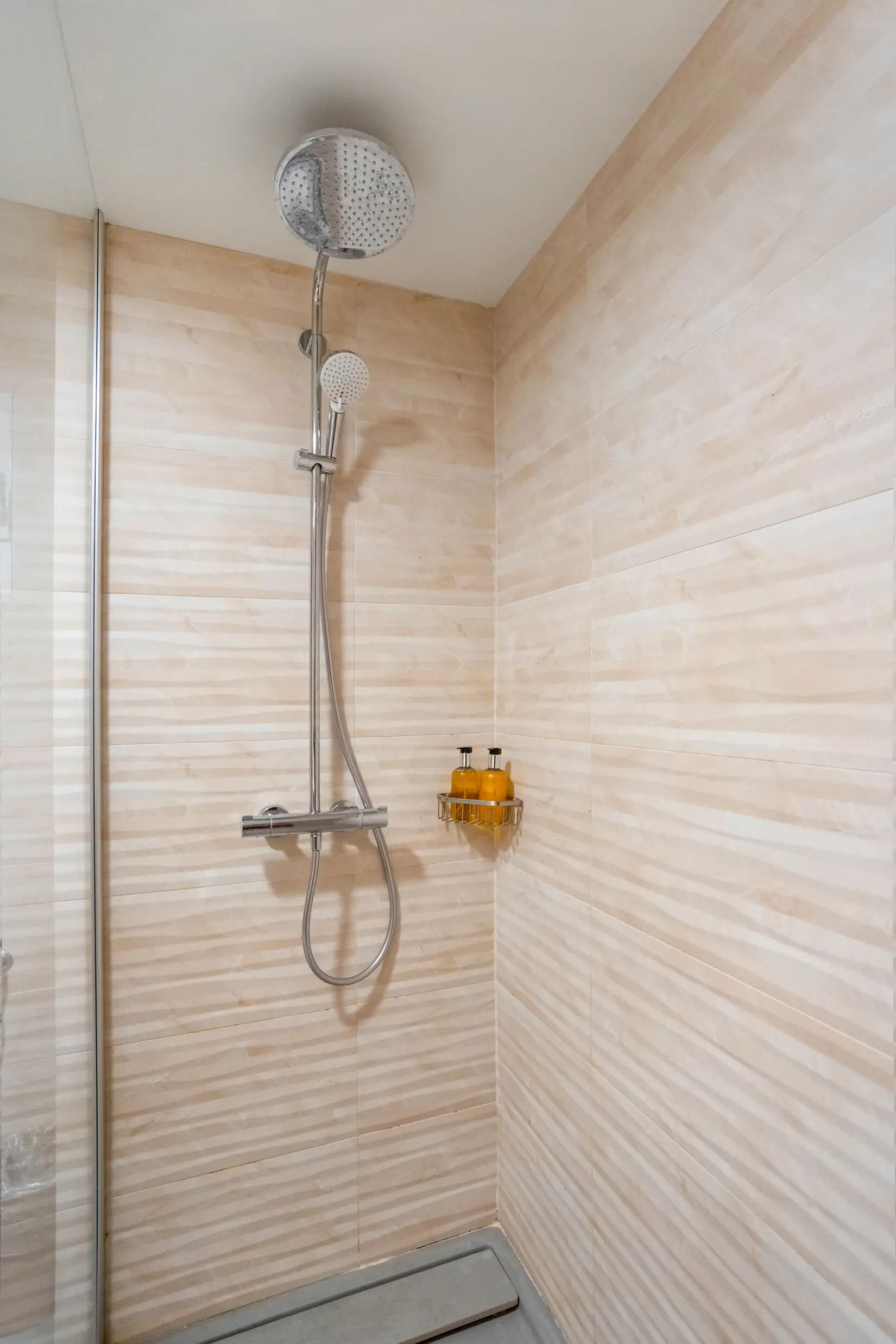Une douche équipée d’un pommeau de douche à main et d’un robinet fixé au mur.