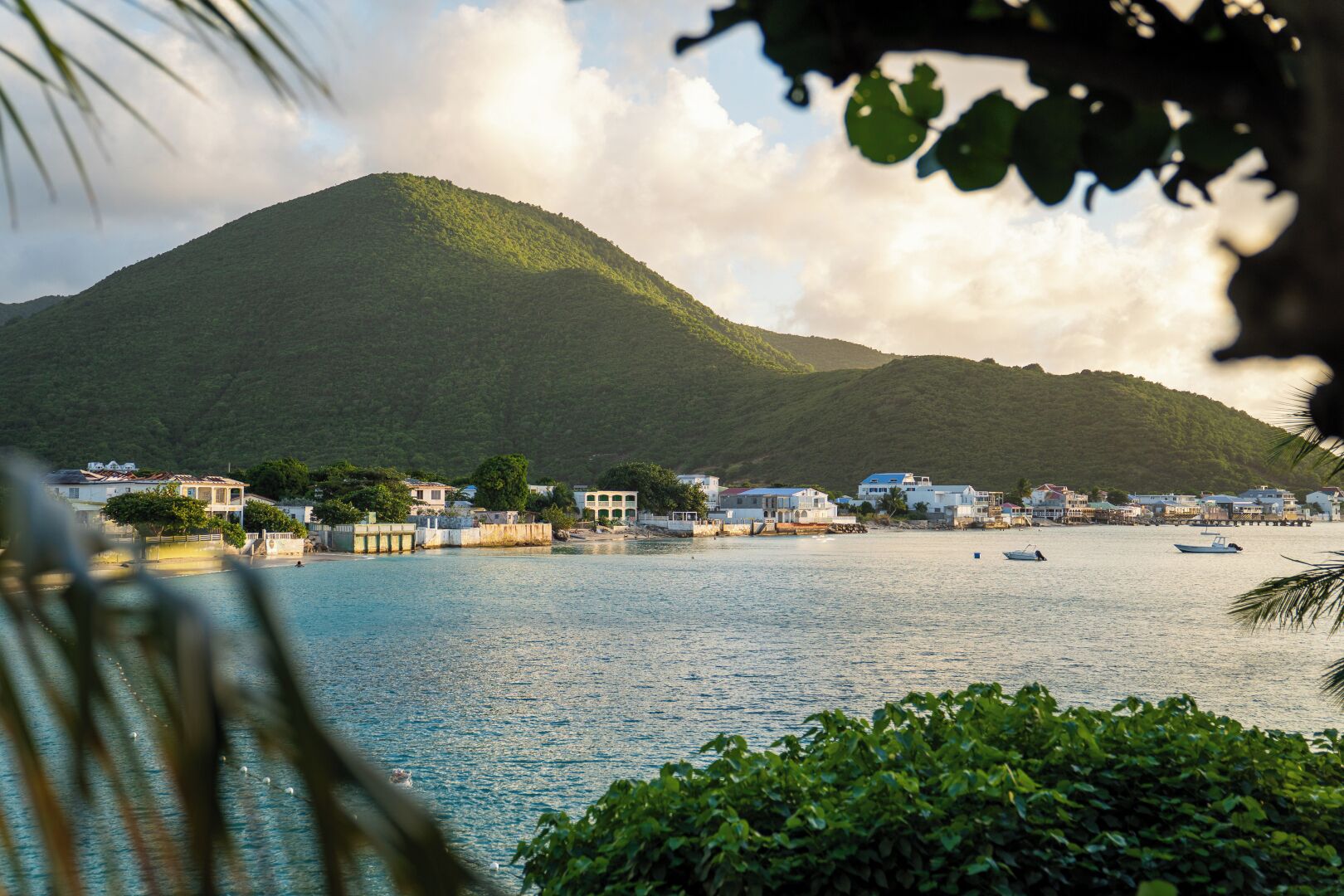 A coastal town with buildings along the waterfront, a hill in the background, and boats on the water.