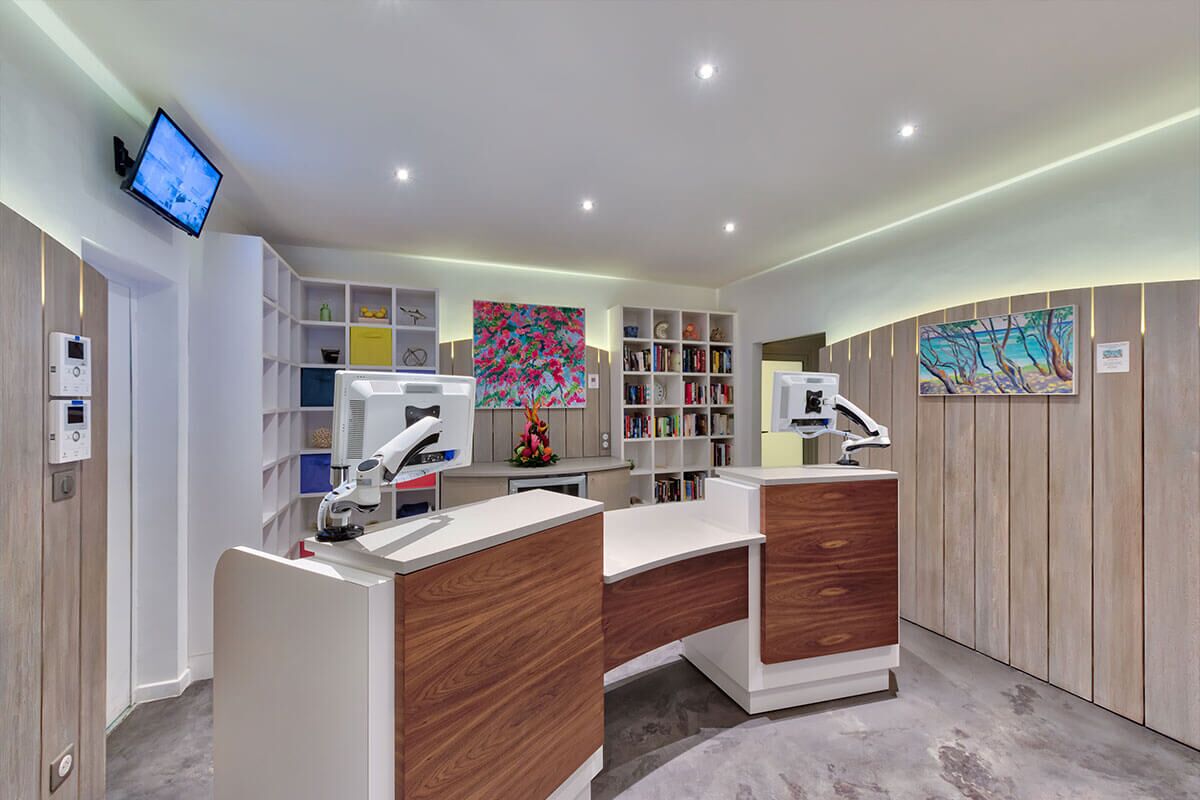 A modern medical office with two desks, a computer, a monitor, and shelves with books and decorative items.