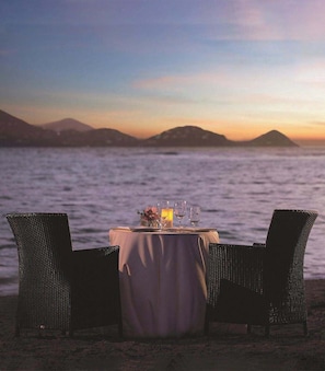 Uma mesa para dois com vista para o mar e montanhas ao longe.