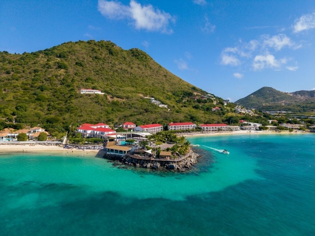 A coastal resort with buildings on a hill, a pier, and clear turquoise waters.