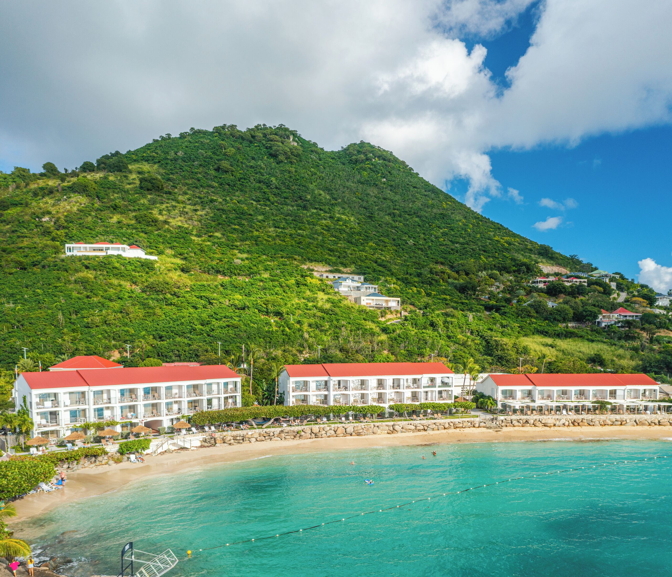 Ein Küstenhotel mit mehreren Gebäuden, einem Strand und einer Bergkulisse.