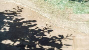 Una playa con agua cristalina y sombras de árboles sobre la arena.