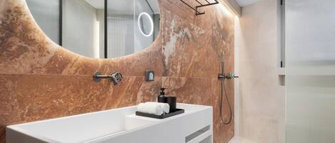 A modern bathroom with a large oval mirror, a white bathtub, and a shower area.