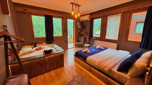 Une pièce confortable avec un lit, un bureau en bois et une chaise. Il y a une fenêtre avec des rideaux, un téléviseur et une vue sur la verdure à l’extérieur.