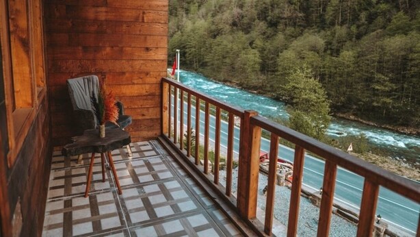 Une cabane en bois dotée d’un balcon donnant sur une rivière et une forêt.