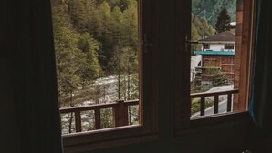 Une salle de bain dotée d’une grande baignoire, de cadres de fenêtres en bois et offrant une vue sur une zone boisée et des montagnes.