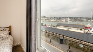 Ein Schlafzimmer mit großem Fenster und Blick auf einen Hafen, ein Bett sowie Schiffe und Gebäude.