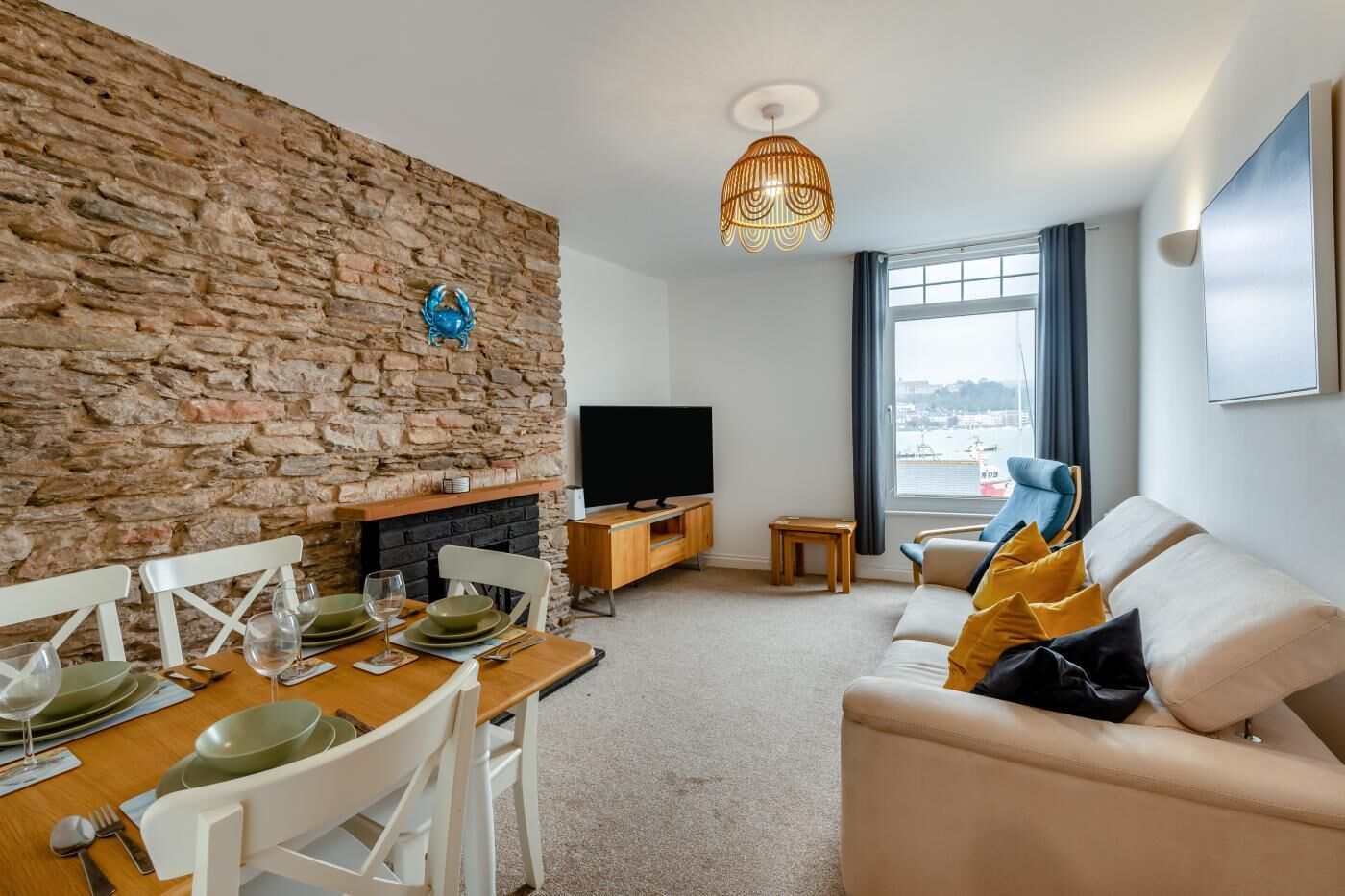 A living room with a stone wall, a fireplace, a TV, a sofa, and a dining area with a table set for two.