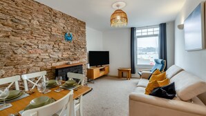 Ein Wohnzimmer mit Steinwand, Kamin, Fernseher, einer Couch und einem Essbereich mit Tisch für zwei Personen.
