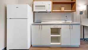 Une cuisine de taille réduite, avec un réfrigérateur blanc, un four à micro-ondes et un évier équipé d’un robinet.