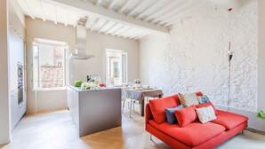 A spacious living area with a red sofa, a kitchen, and a dining area. - The White Lotus Penthouse (Lucca)
