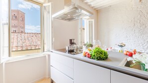 A modern kitchen with a large window, white cabinetry, and a view of a building with a red-tiled roof. - The White Lotus Penthouse (Lucca)
