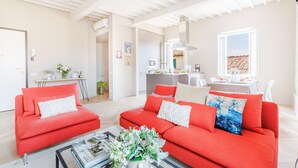A spacious living area with a red sofa set, a coffee table, and a dining area in the background. - The White Lotus Penthouse (Lucca)