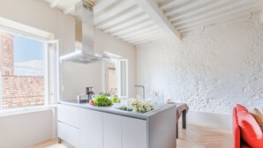 A modern kitchen with a large island, white cabinetry, and a view of a brick building through a window. - The White Lotus Penthouse (Lucca)