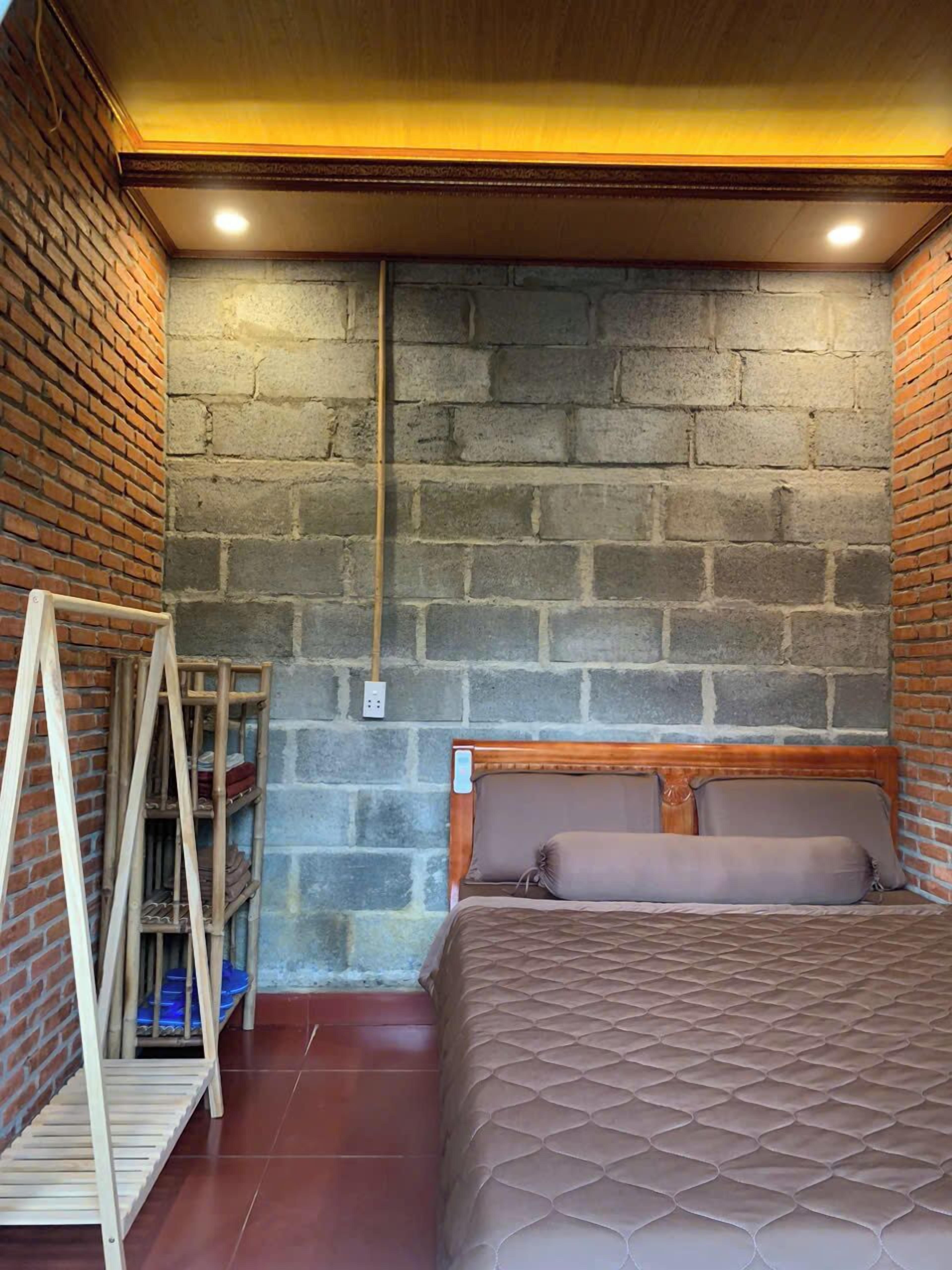 A bedroom with a brick wall, a wooden headboard, a bed with a quilted cover, and a wooden ladder against the wall.