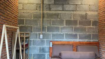 A bedroom with a brick wall, a wooden headboard, a bed with a quilted cover, and a wooden ladder against the wall.