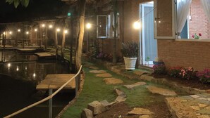 A nighttime view of a resort with a pool, a wooden deck, and a building with an air conditioning unit.