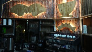 A kitchen with a coffee machine, shelves with supplies, and a rustic wooden wall.
