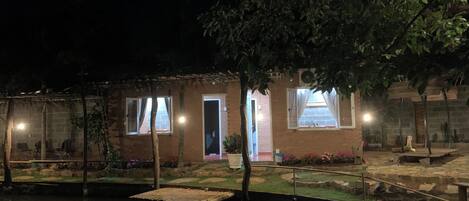 Un pequeño edificio rústico con fachada de ladrillo, techo de paja y un pequeño jardín con un estanque.