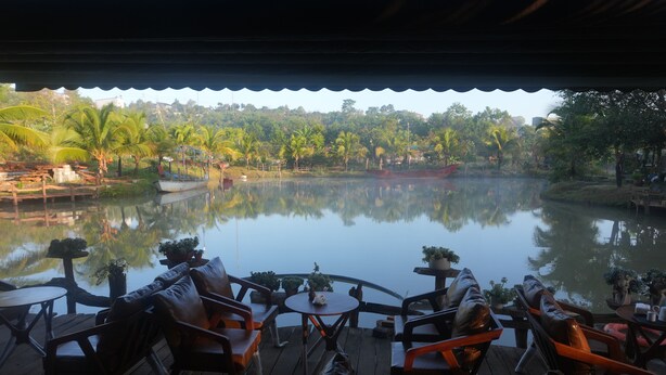 A view from a covered outdoor seating area overlooking a calm lake with reflections of palm trees and a boat.