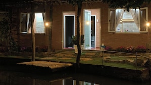 A brick building with multiple windows, some with curtains, and a small garden area with a pond.