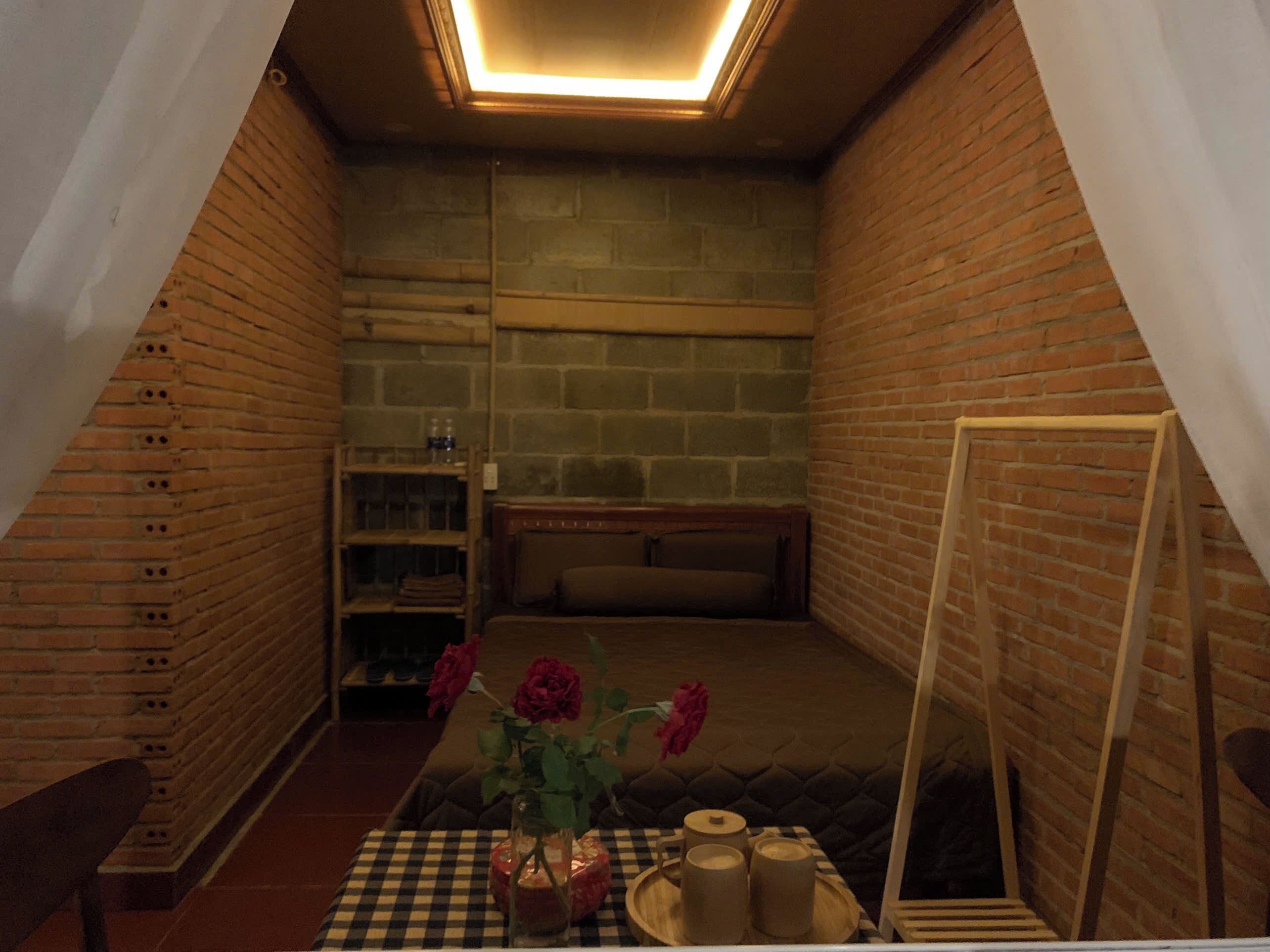A cozy room with a sloped ceiling, brick walls, a bed, a small table with a vase of flowers, and a ladder leaning against the wall.