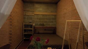 A cozy room with a sloped ceiling, brick walls, a bed, a small table with a vase of flowers, and a ladder leaning against the wall.