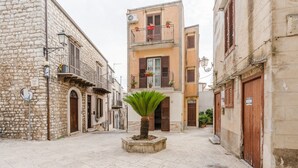 A narrow street with stone buildings, a central palm tree, and a small square. - Room 'Federico 2°' with Mountain View, Wi-Fi and Air Conditioning (Giuliana)