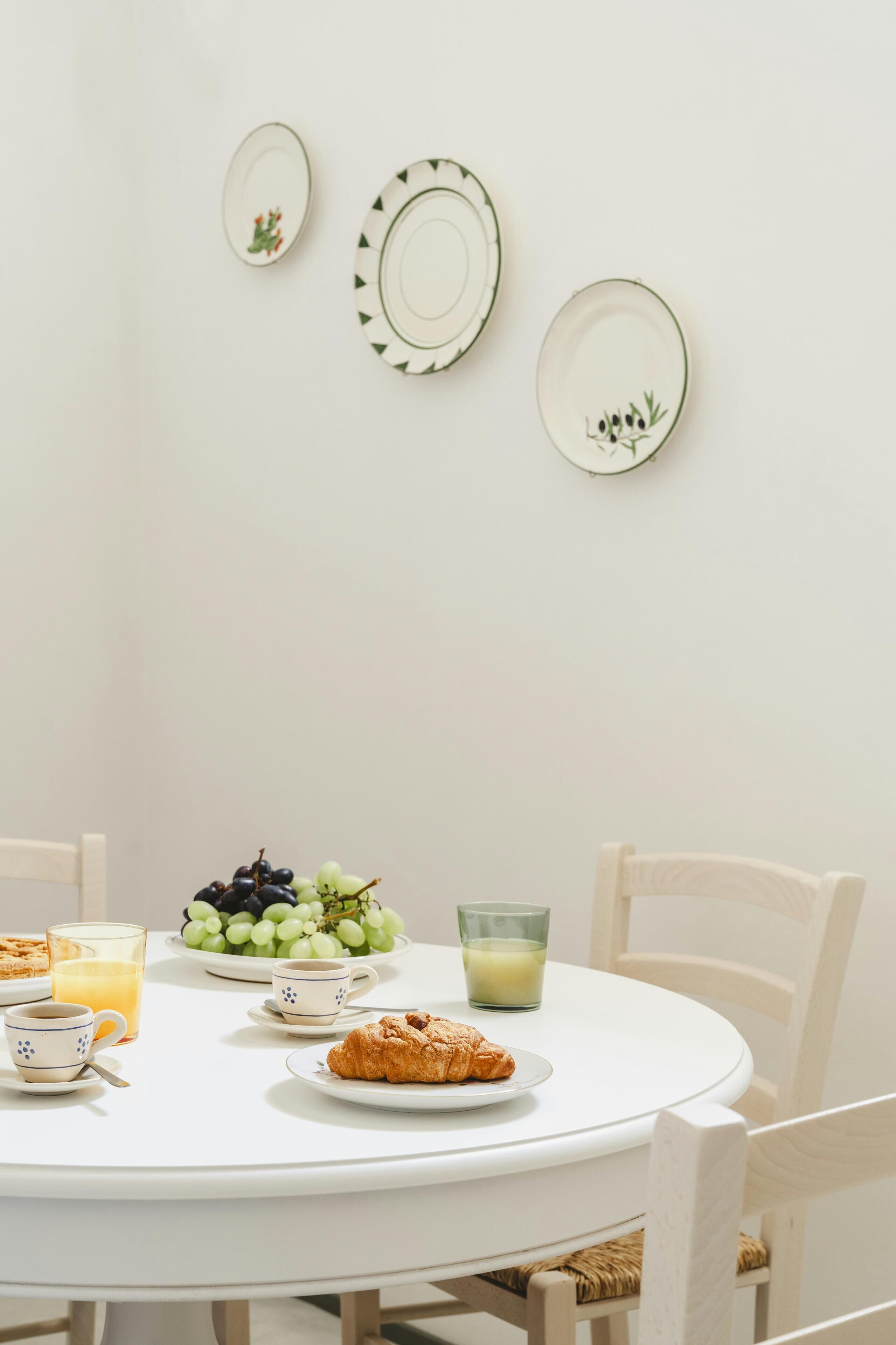 A round dining table with plates, a bowl of grapes, a glass of juice, a croissant, and a cup of coffee.