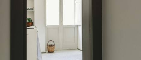 A hallway leading to a room with a large window, a basket, and a plant on a counter.