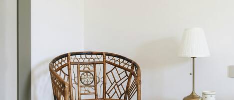 Una silla de mimbre en un rincón de una habitación, junto a un armario verde y una lámpara.